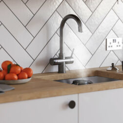 A gun metal swan neck tap in a modern kitchen dispensing boiling water into a mug