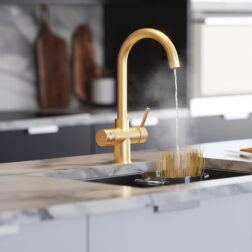 A gold swan neck tap in a modern kitchen dispensing boiling water into a pan of pasta