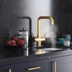 A gold d-neck tap in a modern kitchen running steaming hot water