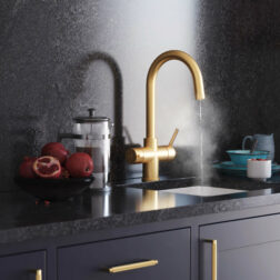 A gold boiling water tap with swan neck running steaming water in dark modern kitchen