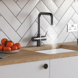 a gun metal D-neck tap running steaming water in a bright kitchen with wooden worktops