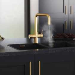 A gold hot water D-neck tap running steaming water in a modern kitchen with black cabinets