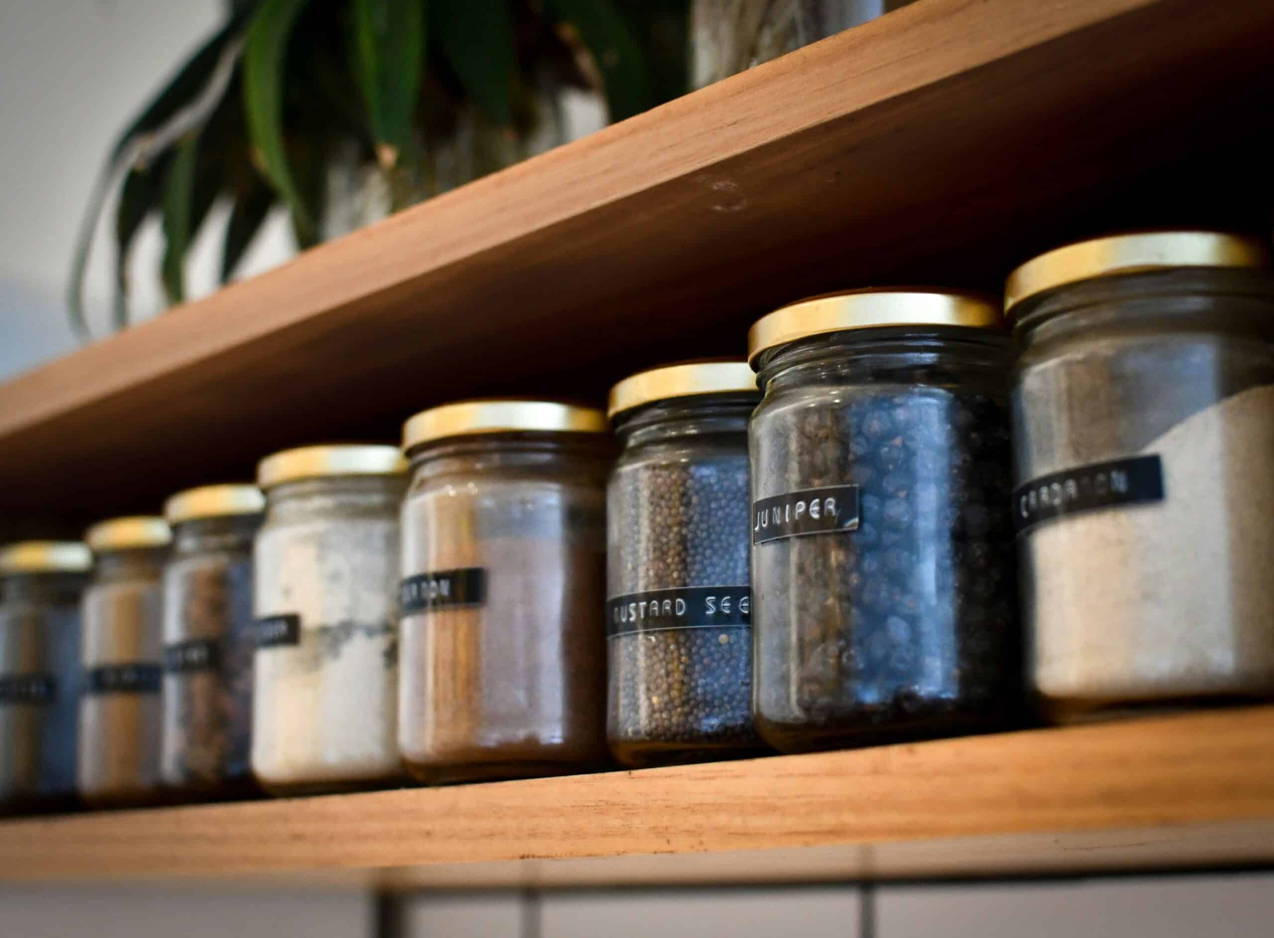 Glass spice jars on a wooden shelf.